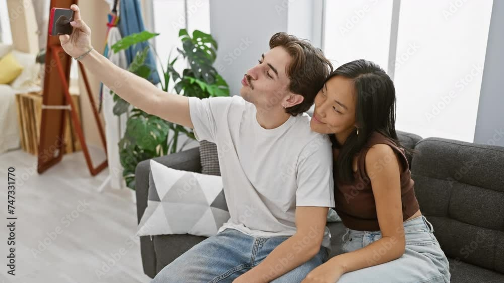 A multicultural couple, woman and man, affectionately take a selfie in their cozy, well-decorated living room. A multicultural couple, woman and man, affectionately take a selfie in their cozy, well-decorated living room.