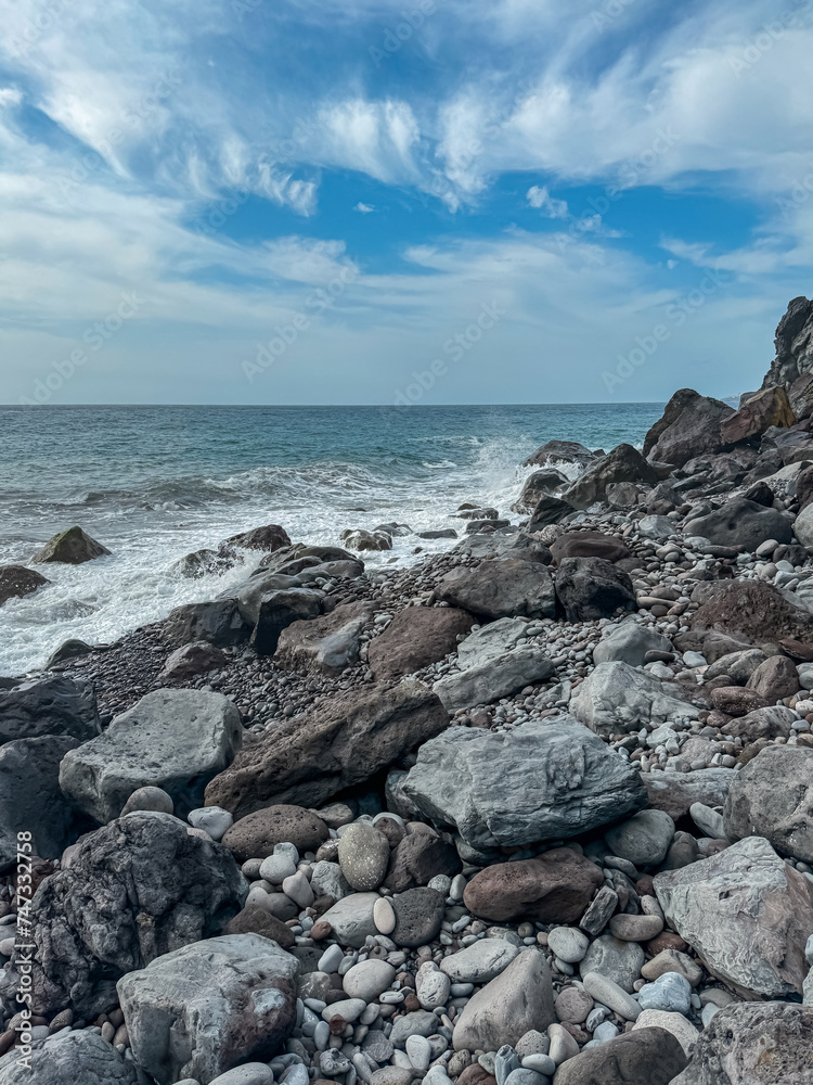 Scenic view of idyllic volcanic black stone beach Praia Garajai, Canico, Madeira island, Portugal, Europe. Sea waves smashing at shoreline of majestic Atlantic Ocean. Dramatic sky. Coastal landscape