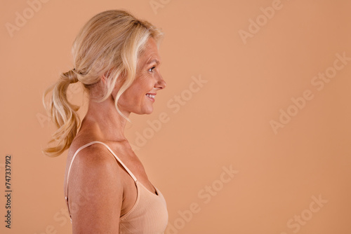Profile side photo of lovely charming retired lady looking empty space promoting anti wrinkles cream isolated on beige color background