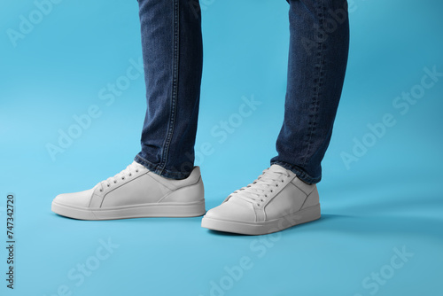 Man wearing stylish white sneakers on light blue background, closeup