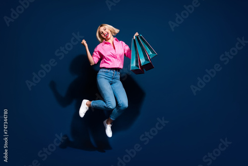 Full body photo of attractive young woman jump raise fists shopping dressed stylish pink clothes isolated on dark blue color background