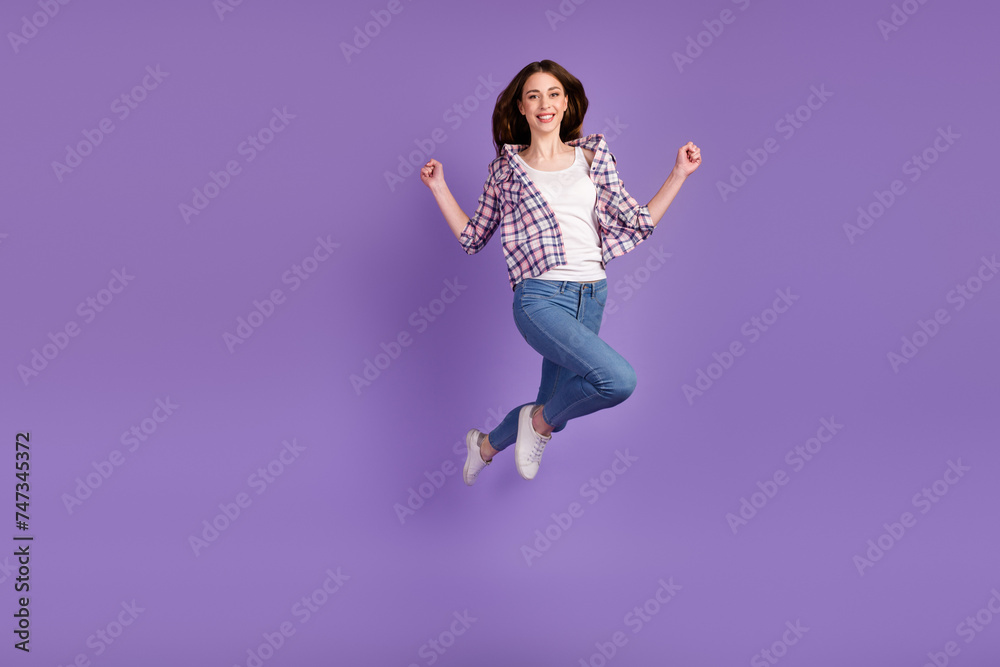 Portrait of sportive active girl in motion jumping over in the air isolated on violet background raise fist up win