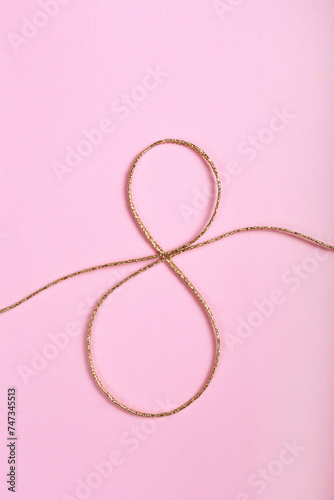 Golden jute twine in the shape of eight as symbol of symbol of women's equality. International women's day concept. Close up, copy space for text, background.