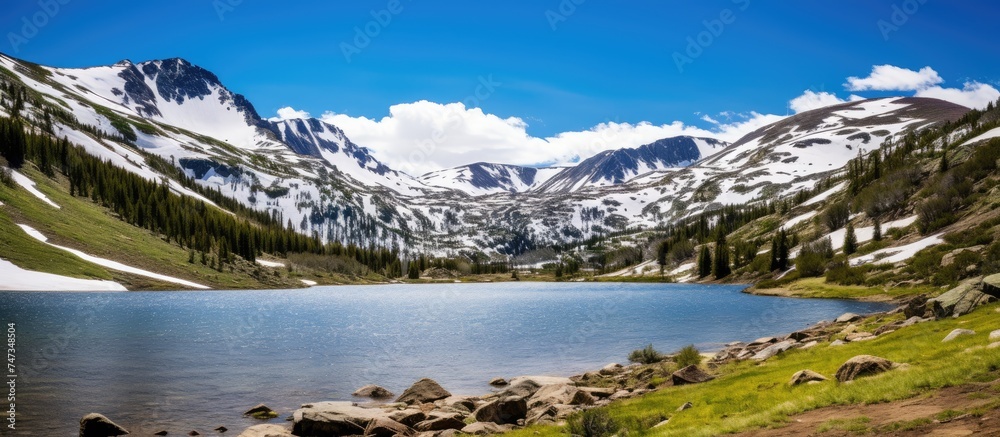 A mountain lake is nestled among snow-capped peaks atop Independence Pass. The tranquil water reflects the stunning snowy landscape, creating a picturesque scene of natural beauty.