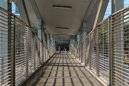 Rear people walk across bridge with light shade to access office