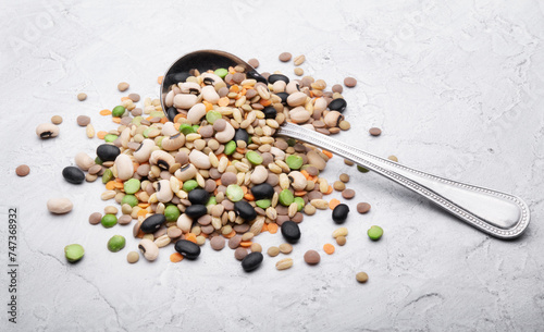 Dried legumes and grains, beans, lentils, barley and peas, vegetable soup mix with old spoon on white plaster background, space for text, close-up.