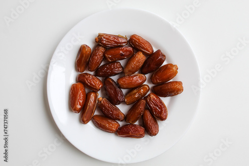 Deglet noor or deglet nour or date palm or dates, in a transparent white plate, isolated on white background, flat lay or top view