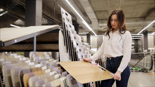 Young woman examines a laminate floor in a hardware store. Woman holding parquet board panel sample. SPC flooring