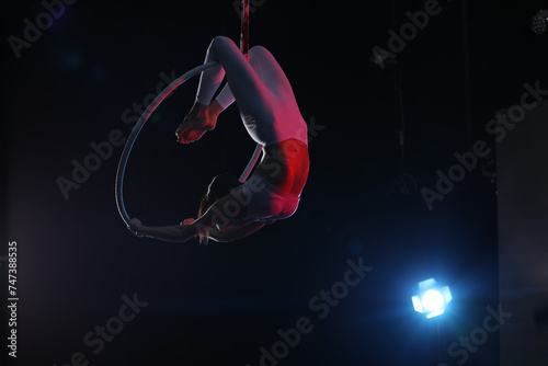 Young woman performing acrobatic element on aerial ring against dark background photo