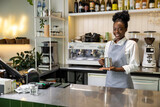 Smiling multicultural woman barista making coffee standing at counter in cafe