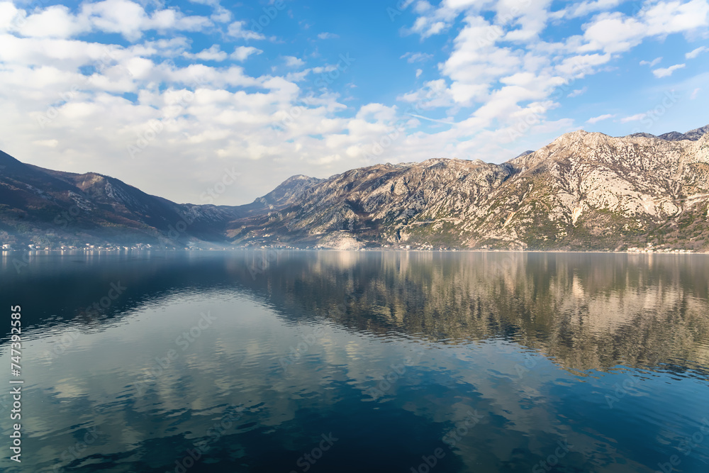Mountains over Bay of Kotor (Boka kotorska). Misty morning. Calm water and sky reflected in water surface. Scenic nature background or wallpaper. Kotor, Montenegro