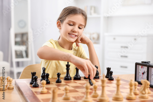 Cute girl playing chess at table in room
