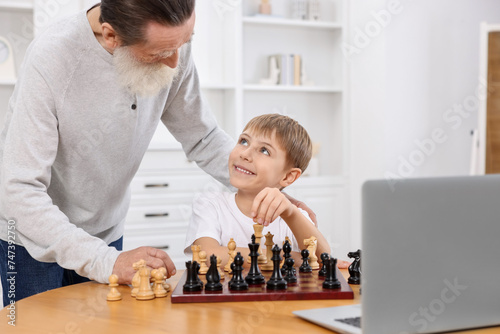 Grandfather teaching his grandson to play chess following online lesson at home