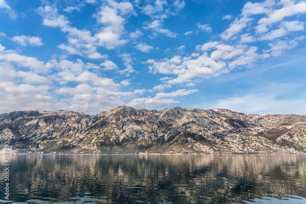 Mountains over Bay of Kotor (Boka kotorska). Calm water and sky reflected in water surface. Scenic nature background or wallpaper. Kotor, Montenegro
