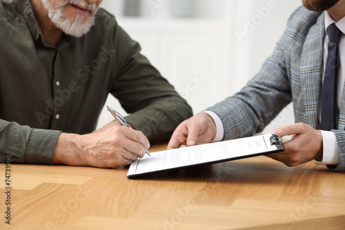 Notary showing senior man where to sign Last Will and Testament at wooden table indoors  closeup