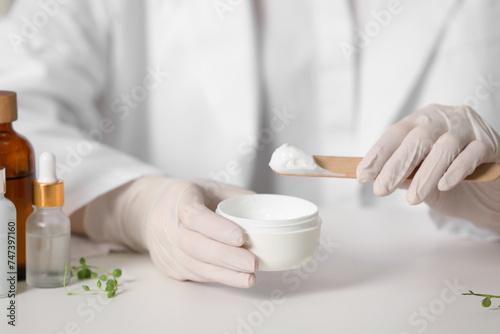 Dermatologist with jar testing cosmetic product at white table, selective focus
