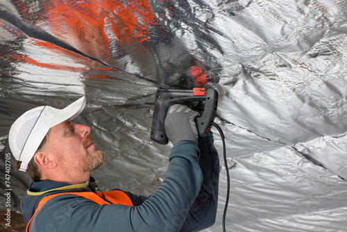 a worker in a vest and cap is fixing the vapor barrier on the ceiling