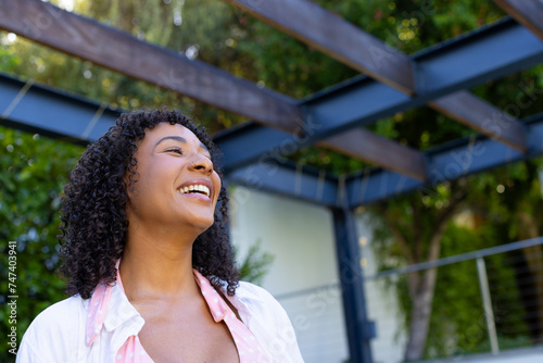 Young biracial woman smiles brightly, looking upwards outdoors at home with copy space