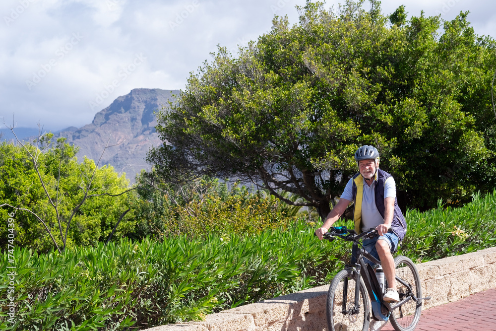 Happy active cyclist senior man wearing bicycle helmet enjoys beautiful day outdoors. Smiling elderly grandfather running in nature, retired healthy lifestyle