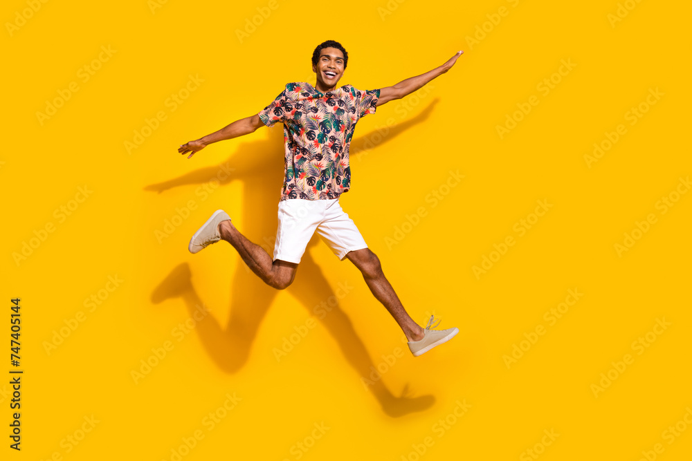 Full length photo of carefree cool guy dressed print t-shirt jumping high arms sides empty space isolated yellow color background