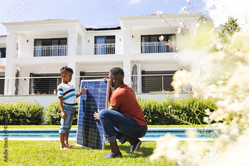African American father and son discuss a solar panel by a poolside photo