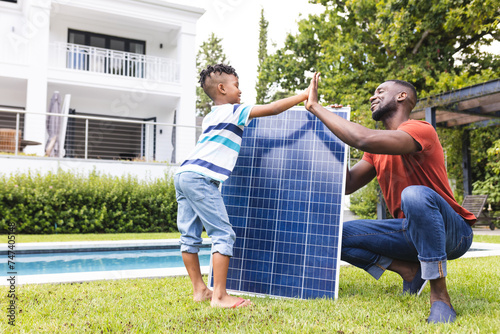 African American father and son install a solar panel near a pool with copy space photo