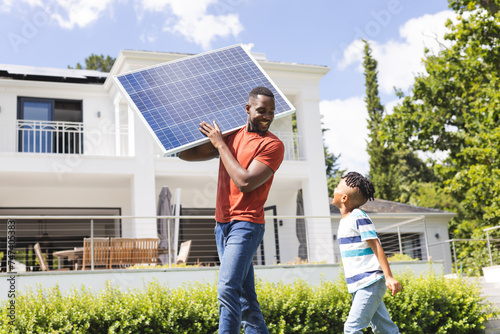 African American father carries a solar panel while a son walks beside him photo