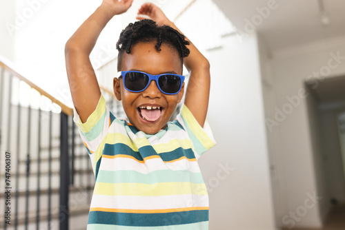 African American boy wears blue sunglasses and a striped shirt, arms raised in excitement