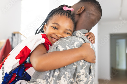 African American girl embraces a soldier, her smile radiates joy, with an American flag photo