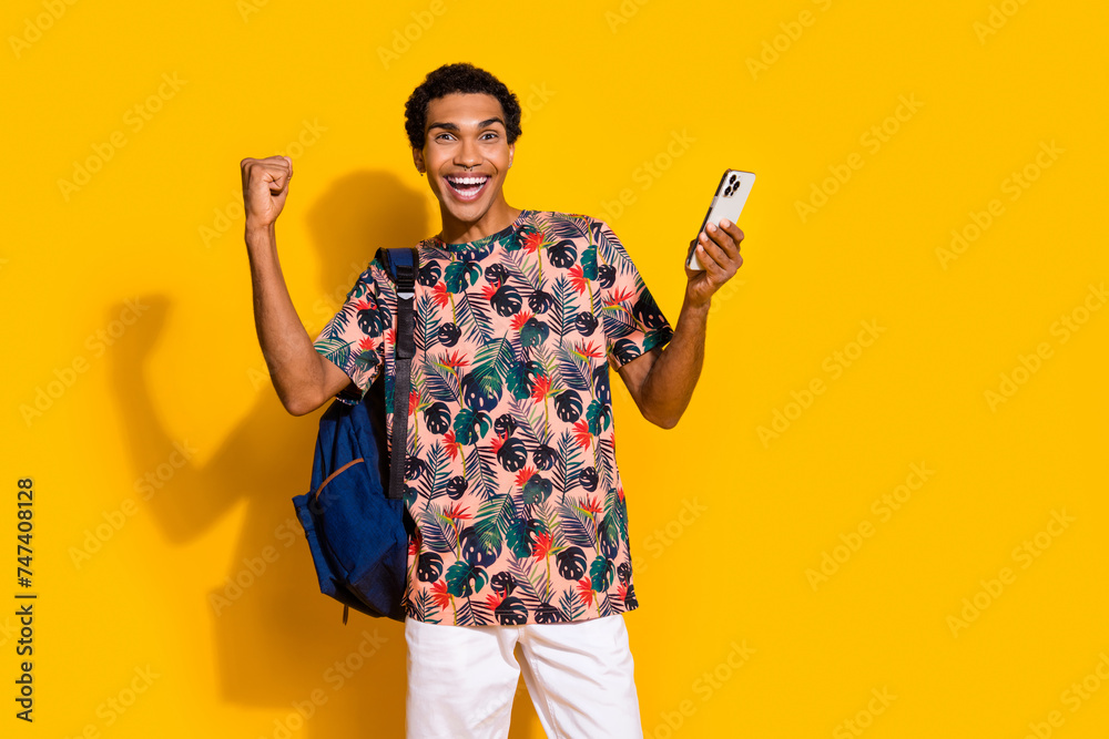 Photo of young guy raised fist up winning free access for student premium application smartphone isolated on yellow color background