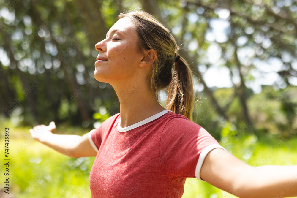 Young woman with her arms outstretched enjoys the sun in a green park Young woman with her arms outstretched enjoys the sun in a green park