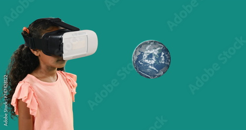 Biracial child with a VR headset stands before a floating graphic of Earth
