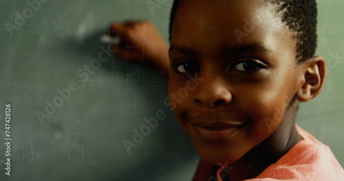 African American child writes on a chalkboard, turning to smile at the camera