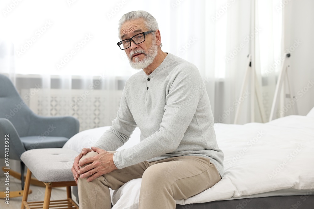 Arthritis symptoms. Man suffering from pain in knee on bed at home Arthritis symptoms. Man suffering from pain in knee on bed at home
