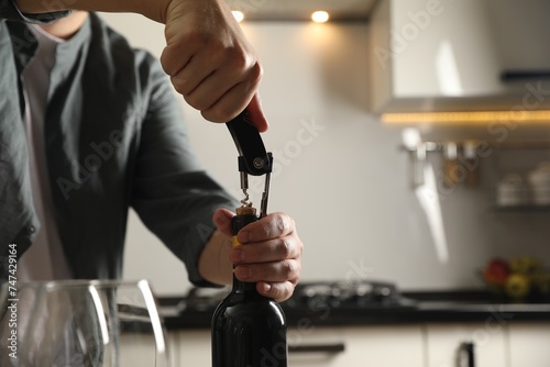 Man opening wine bottle with corkscrew indoors, closeup. Space for text photo