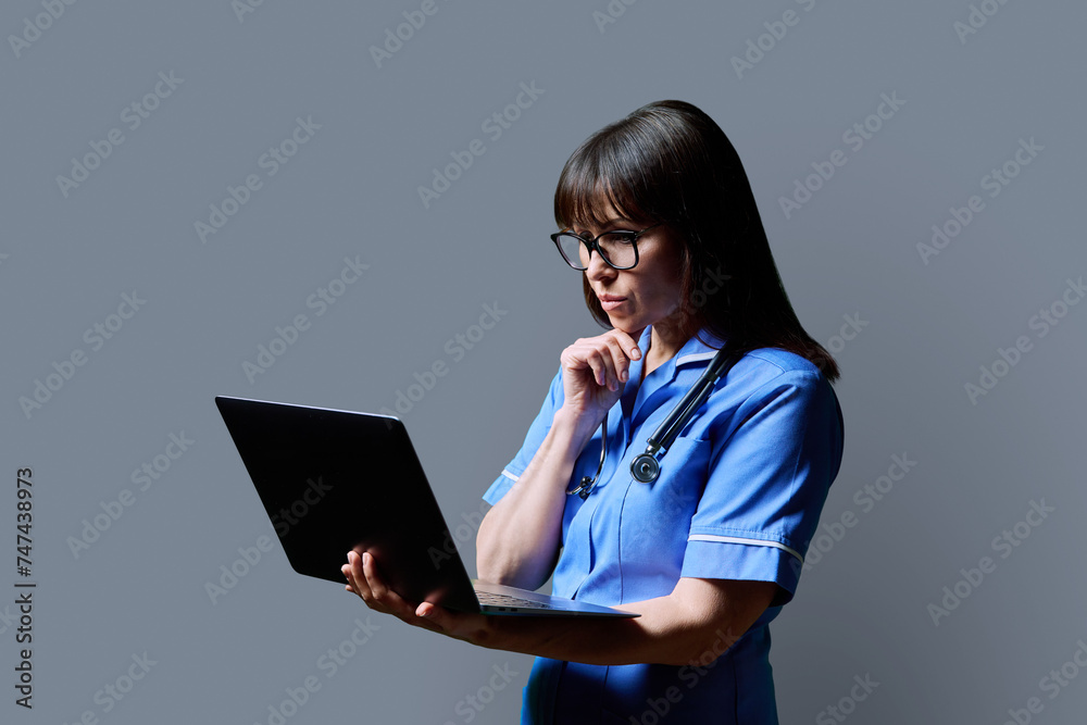 Female nurse using laptop, profile view on gray studio background Female nurse using laptop, profile view on gray studio background
