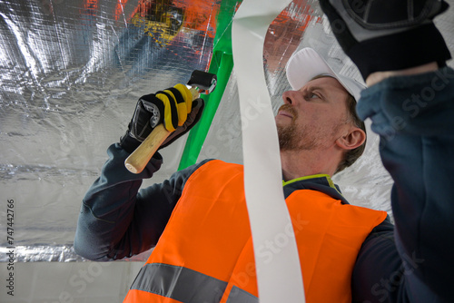 the construction worker uses aluminum tape and they had a roller for vapor barrier joints on the ceiling photo