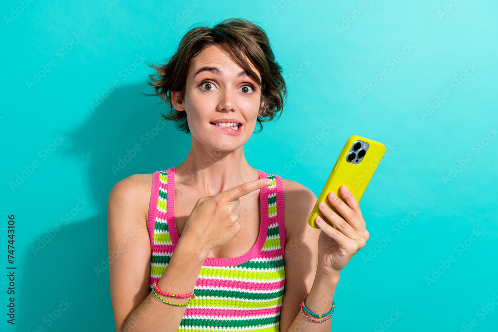 Portrait of lovely nice person biting lips indicate finger arm hold smart phone instagram x tiktok isolated on turquoise color background Portrait of lovely nice person biting lips indicate finger arm hold smart phone instagram x tiktok isolated on turquoise color background