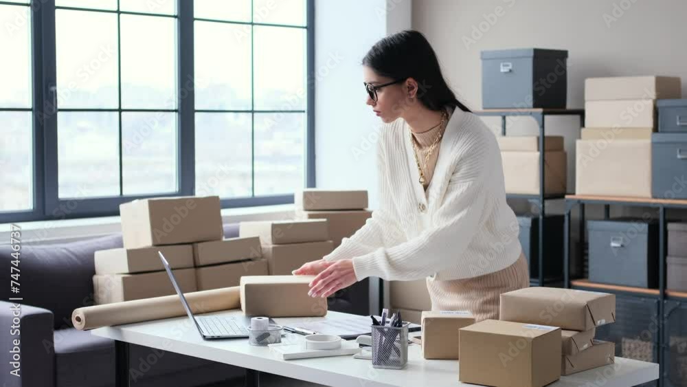 Serious Caucasian female merchant preparing cardboard box with order from online shop for sending to consumer, working in warehouse. Serious Caucasian female merchant preparing cardboard box with order from online shop for sending to consumer, working in warehouse.
