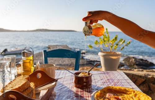 Close up of breakfast served on a typically Greek tavern table at sunrise with hand pouring honey into a yogurt with the Aegean Sea in the background photo