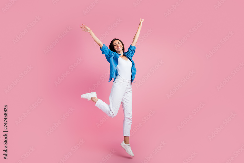 Full size photo of carefree peaceful gorgeous girl dressed blue shirt white trousers fly hold arms up isolated on pink color background Full size photo of carefree peaceful gorgeous girl dressed blue shirt white trousers fly hold arms up isolated on pink color background