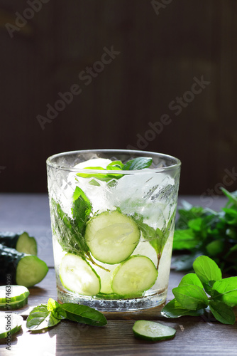 Cucumber ice flavored with mint water ot cocktail on wooden table on dark background, vertical, fresh spring and summer detox drinks, natural healthy food concept