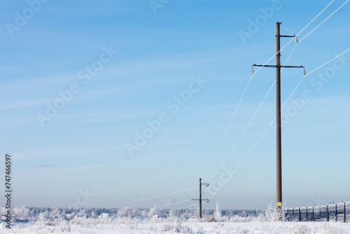 electric high-voltage pylons in the winter landscape with snow-covered trees , clear cold morning