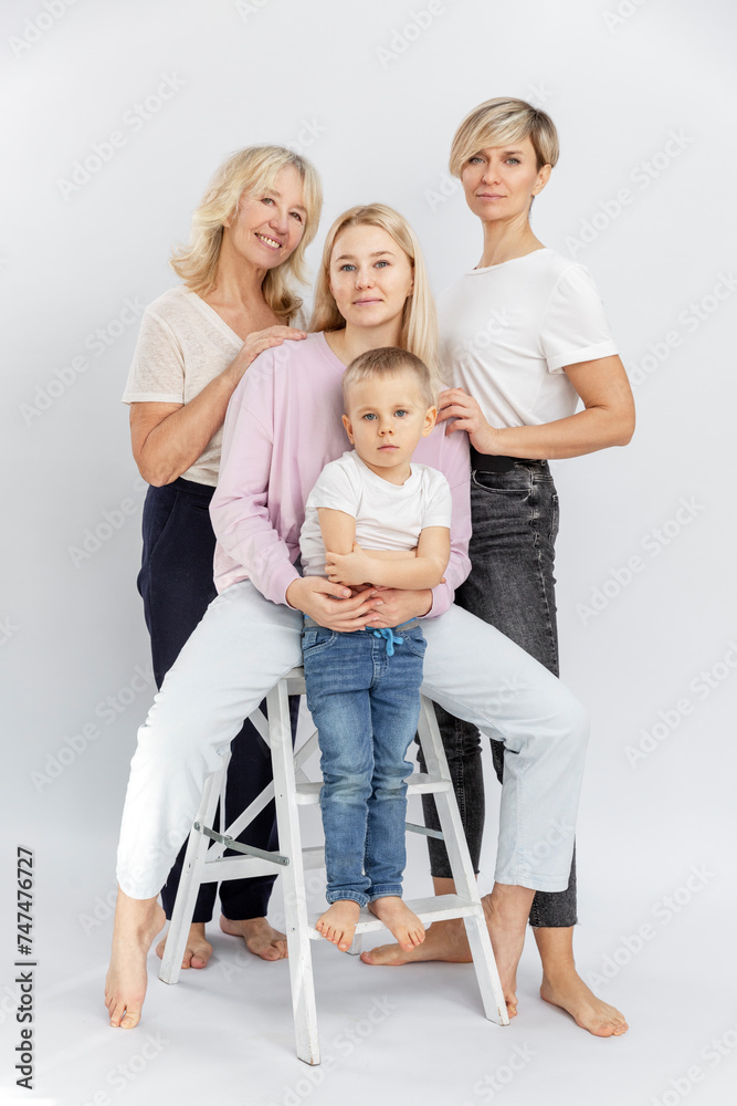 Happy smiling family. Three generations of women and a little boy in white T-shirts and jeans. Full height. Love and tenderness. White background. Vertical. Happy smiling family. Three generations of women and a little boy in white T-shirts and jeans. Full height. Love and tenderness. White background. Vertical.