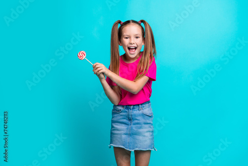 Photo of funky cute positive good mood schoolgirl wear pink t-shirt hold lollipop fooling around isolated on teal color background