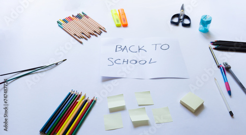 School accessories on a white background and white paper in the middle with "back to school' text on it. View from above, top view. Concept for back to school, School supplies. Copy space