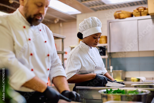 Black female chef and her coworker preparing food in kitchen in restaurant.