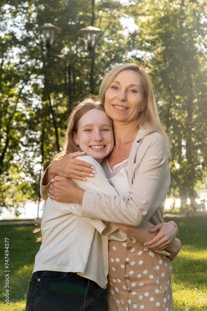 Fototapeta premium Mother embraces smiling daughter creating heartwarming scene. Positive girl and loving parent share moment of pure happiness