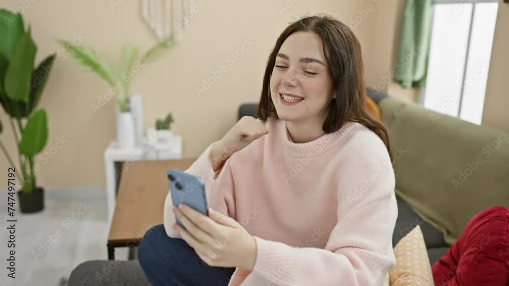Smiling young woman using smartphone in a cozy, modern living room, conveying connection and leisure.