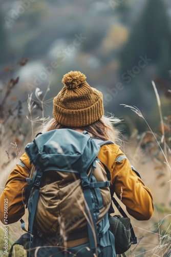 A woman with a backpack walking through a field. Suitable for outdoor and adventure themes © Fotograf